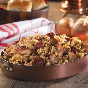 a bowl of jambalaya with bread rolls in the background