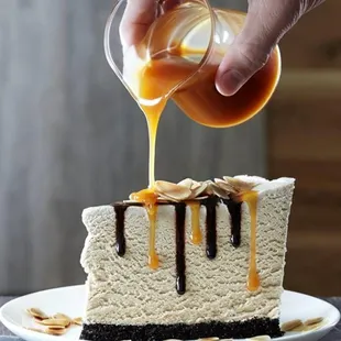 a slice of cheesecake being drizzled with caramel