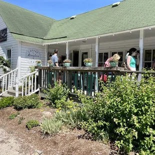 Front entrance and exterior of shop with front porch seating. Behind the shop on other side is more seating and a flower garden.