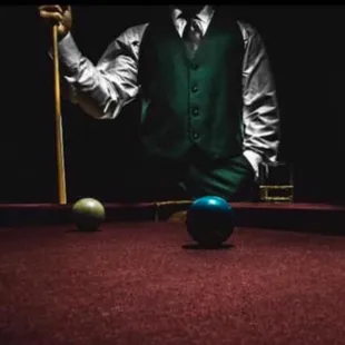 a man in a vest and tie playing pool