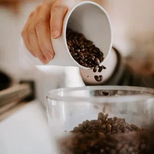 a person pouring coffee beans into a cup