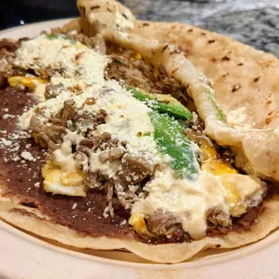 Loaded Baleada. Homemade Honduran flour tortilla, refried beans, eggs, sour cream, cheese, choice of meat (carnitas here), and avocado. $10.