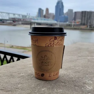 a coffee cup on a ledge overlooking a river