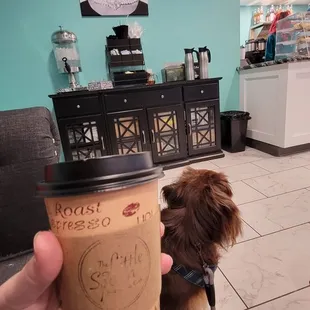 a person holding a cup of coffee with a dog on a leash