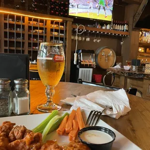 a plate of buffalo wings, carrots, celery, and a glass of beer