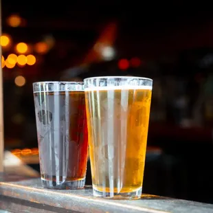 two glasses of beer sitting on a window sill