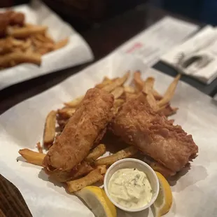 a plate of fish and chips with a side of lemon wedges