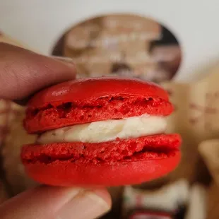 a hand holding a red velvet macaron