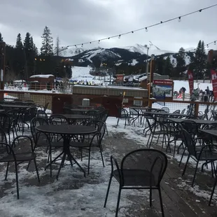 tables and chairs on a deck with mountains in the background