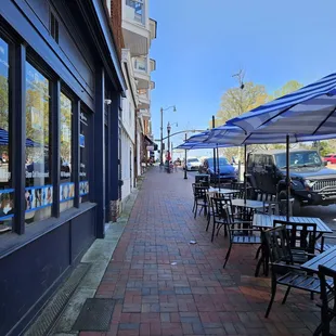 a sidewalk with tables and umbrellas