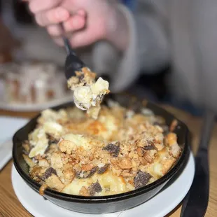 a person holding a fork over a dish of macaroni and cheese