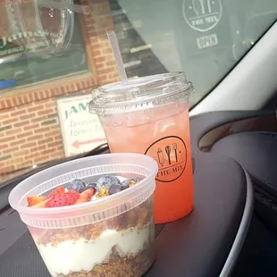 two cups of fruit and yogurt on the dashboard of a car