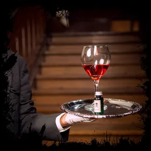 a man holding a tray with a glass of wine