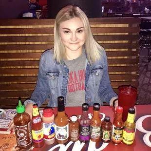 a woman sitting at a table with hot sauces