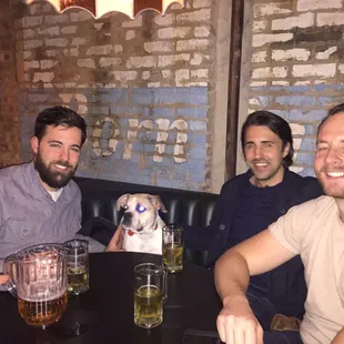 three men sitting at a table with a dog