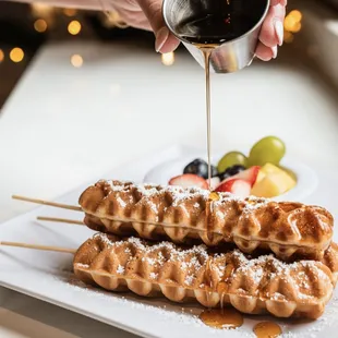 a person pouring syrup over waffles