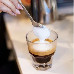 a person scooping milk into a cup of coffee