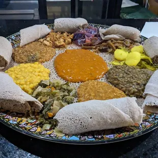 A plate of ten different dishes- lentils, mushrooms, split peas, cabbage and more. With spongy sourdough bread rolls.