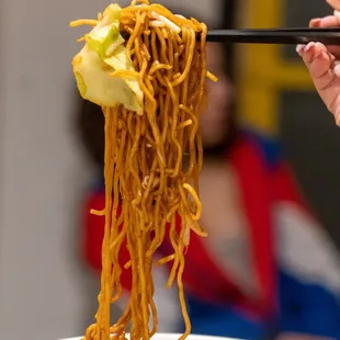 a person holding chopsticks over a bowl of noodles