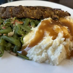 Meatloaf, dinner, green beans with ham, and whipped potatoes with brown gravy.