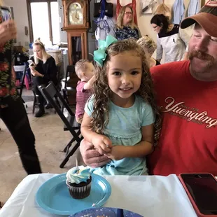 a man and a little girl sitting at a table with a cupcake