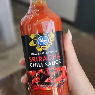 a hand holding a bottle of chili sauce