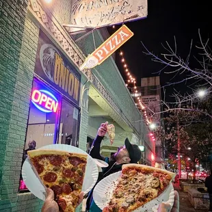 two people holding up slices of pizza