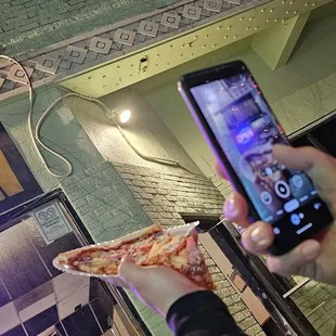 a person taking a picture of a slice of pizza
