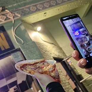 a person taking a picture of a slice of pizza
