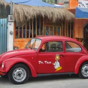 a red vw beetle parked in front of a restaurant