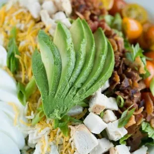 a salad with chicken, lettuce, tomatoes, cheese, and avocado