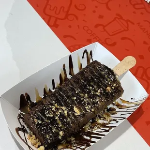 Cookies and cream paleta dipped in milk chocolate drizzled with dark chocolate/caramel and covered with peanuts.