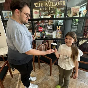 Robert handing off a fresh lavender latte to Maya