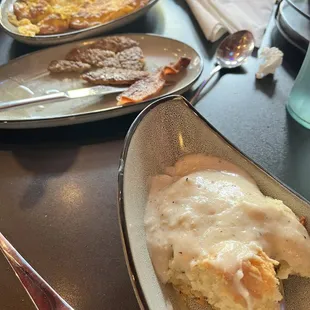 Eggs, sausage, bacon in background. Biscuit &amp; gray in foreground.