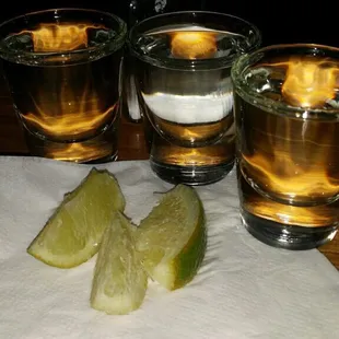 three shot glasses with lime slices on a napkin