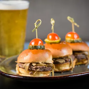 a plate of hamburgers with pickles and a glass of beer