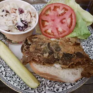 Softshell crab sandwich with lettuce and tomato, coleslaw and pickle on the side. Carryout order plated at home.