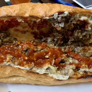 Opened cheesesteak with ketchup added.