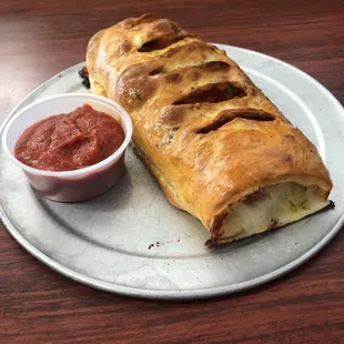 a long loaf of bread with a side of tomato sauce