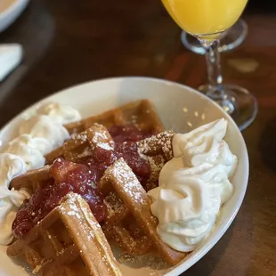 Waffles with whipped cream and strawberry compote added and a Life&apos;s a Peach mimosa