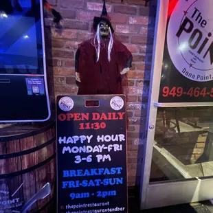 a man dressed as a witch standing next to a sign