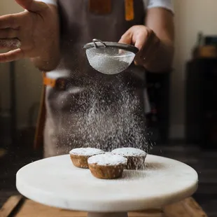a baker sprinkling sugar on a pastry