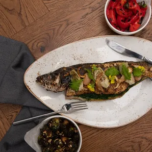 a fish on a plate with a fork and a bowl of vegetables