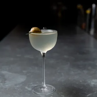 a glass of white wine with a olive garnish