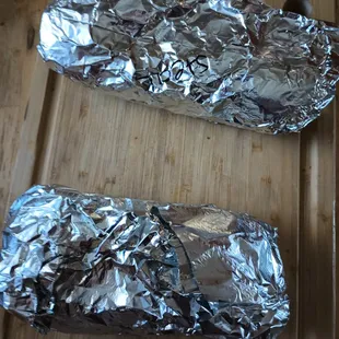 two wrapped sandwiches on a cutting board