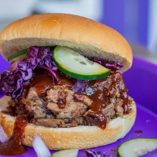a purple plate with a pulled pork sandwich on it