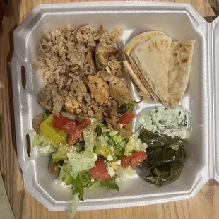 Chicken platter with rice Greek salad and grape leaves, pita bread.