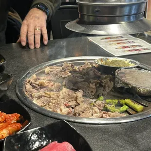 Meat cooking, along with a side of steamed egg, asparagus, and sweet corn in some tasty cheese sauce.