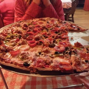 a woman sitting at a table with a large pizza