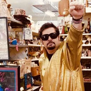 a man in a gold jacket and sunglasses holding up a glass